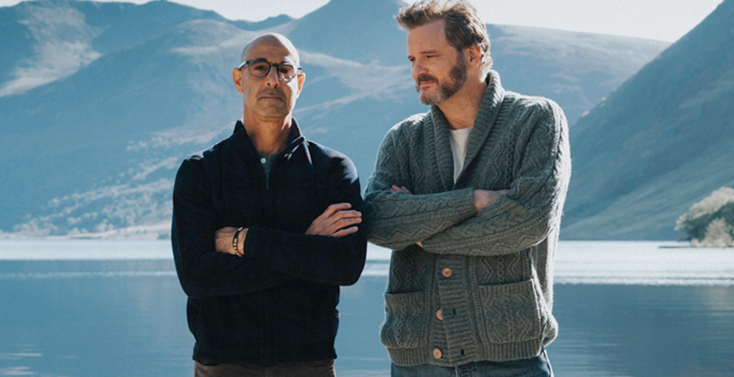 Stanley Tucci and Colin Firth stand side-by-side in from of a lake in a still from Supernova