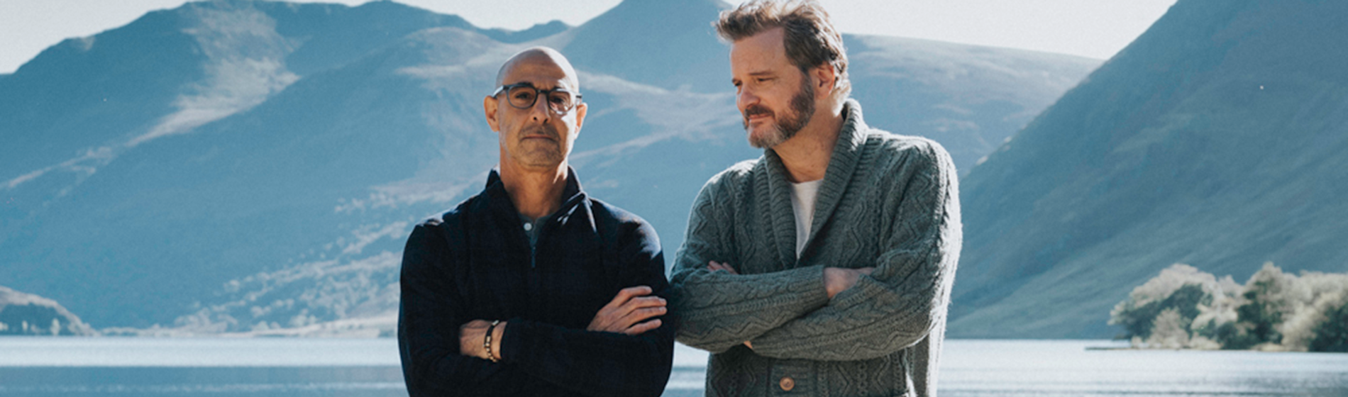 Stanley Tucci and Colin Firth stand side-by-side in from of a lake in a still from Supernova