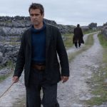 The Banshees of Inisherin still with Colin Farrell walking toward camera and Brendan Gleeson walking away in the distance on a gray Irish dirt road