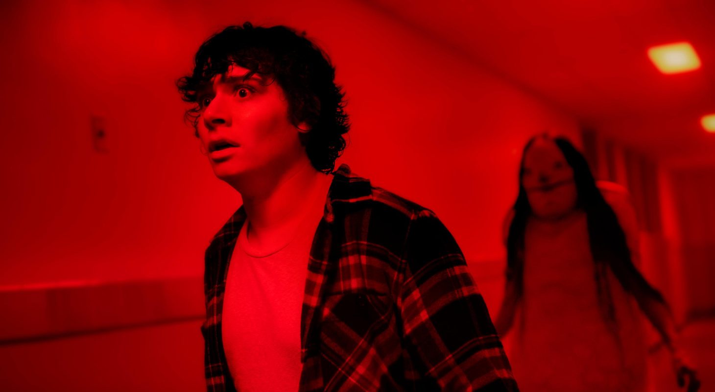 A male teen (l) and a large woman (r) in a red hallway in Scary Stories to Tell in the Dark