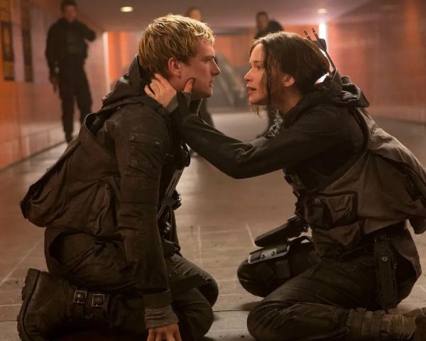 Katniss (Jennifer Lawrence - R) comforts Peeta (Josh Hutcherson - L) in a red walled tunnel