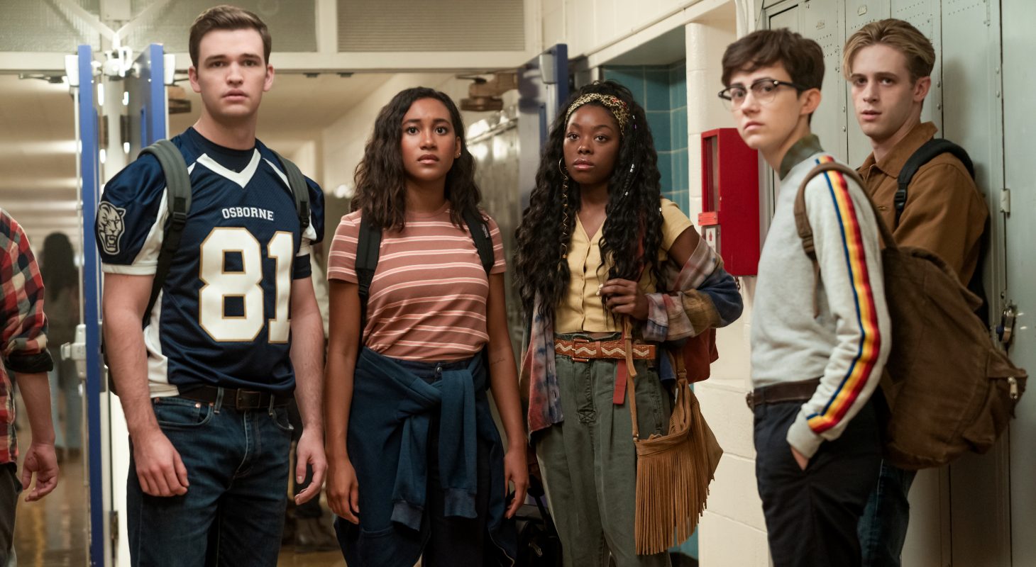 Five teens stand in a hallway, looking at the camera