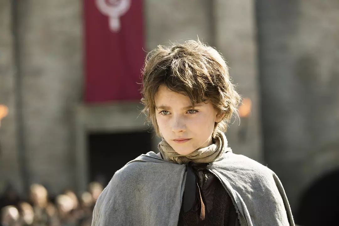 A young girl with a boy's haircut poses in front of a medieval castle