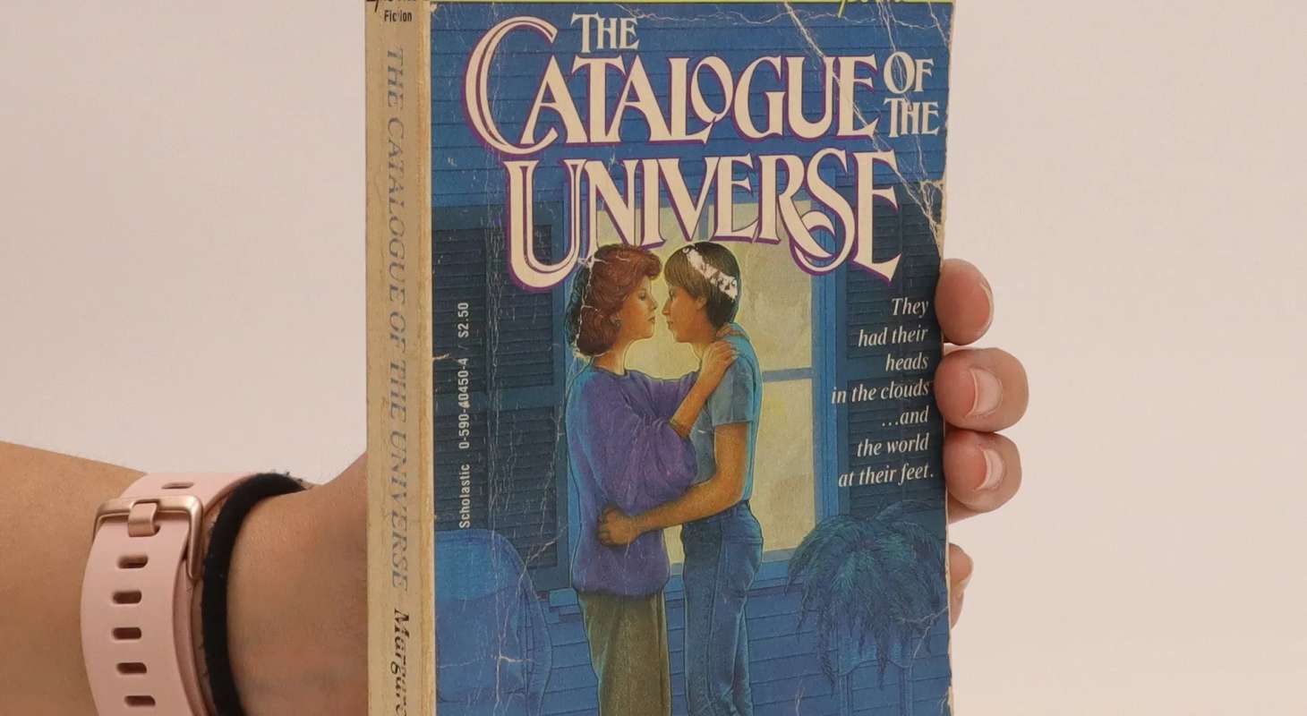 A hand wearing a pink watch holding the paperbook of The Catalogue of the Universe