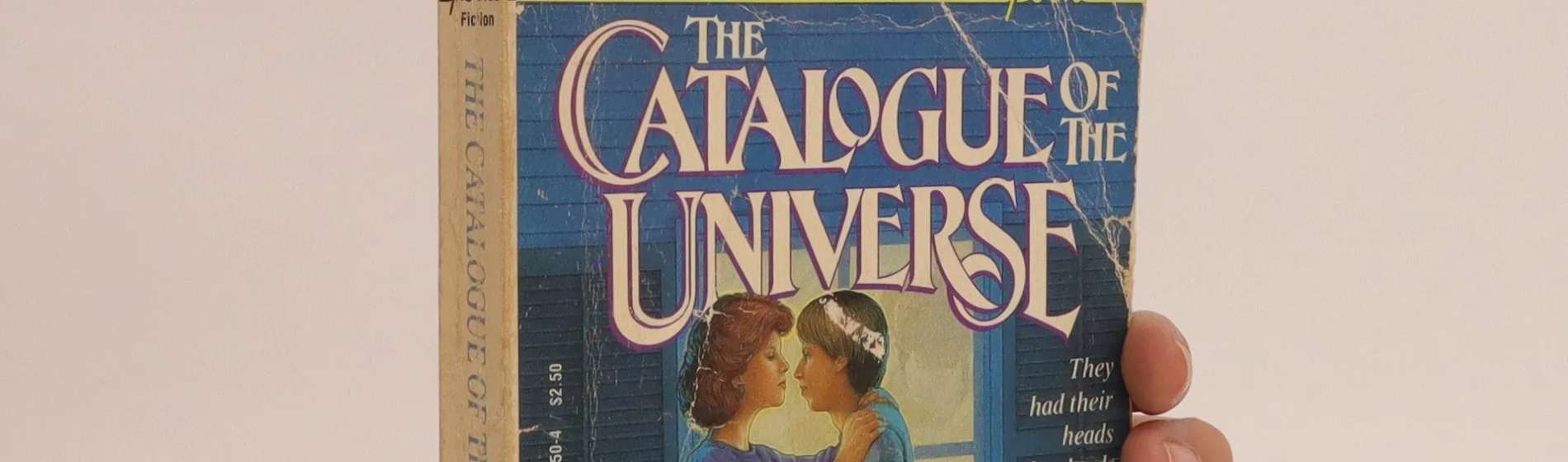 A hand wearing a pink watch holding the paperbook of The Catalogue of the Universe