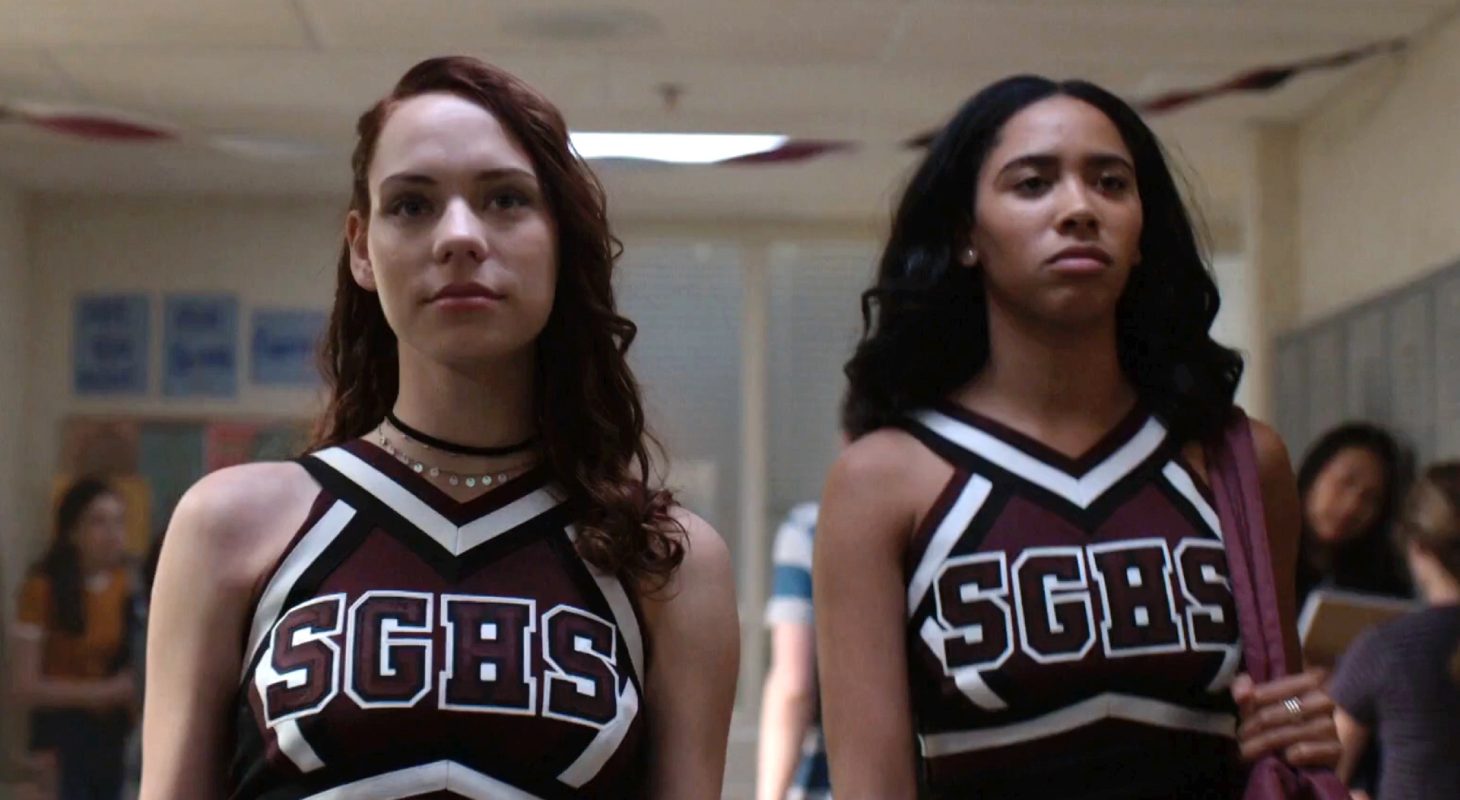 Beth (Marlo Kelly) and Abby (Herizen Guardiola) walk down the school hallway wearing cheerleading uniforms
