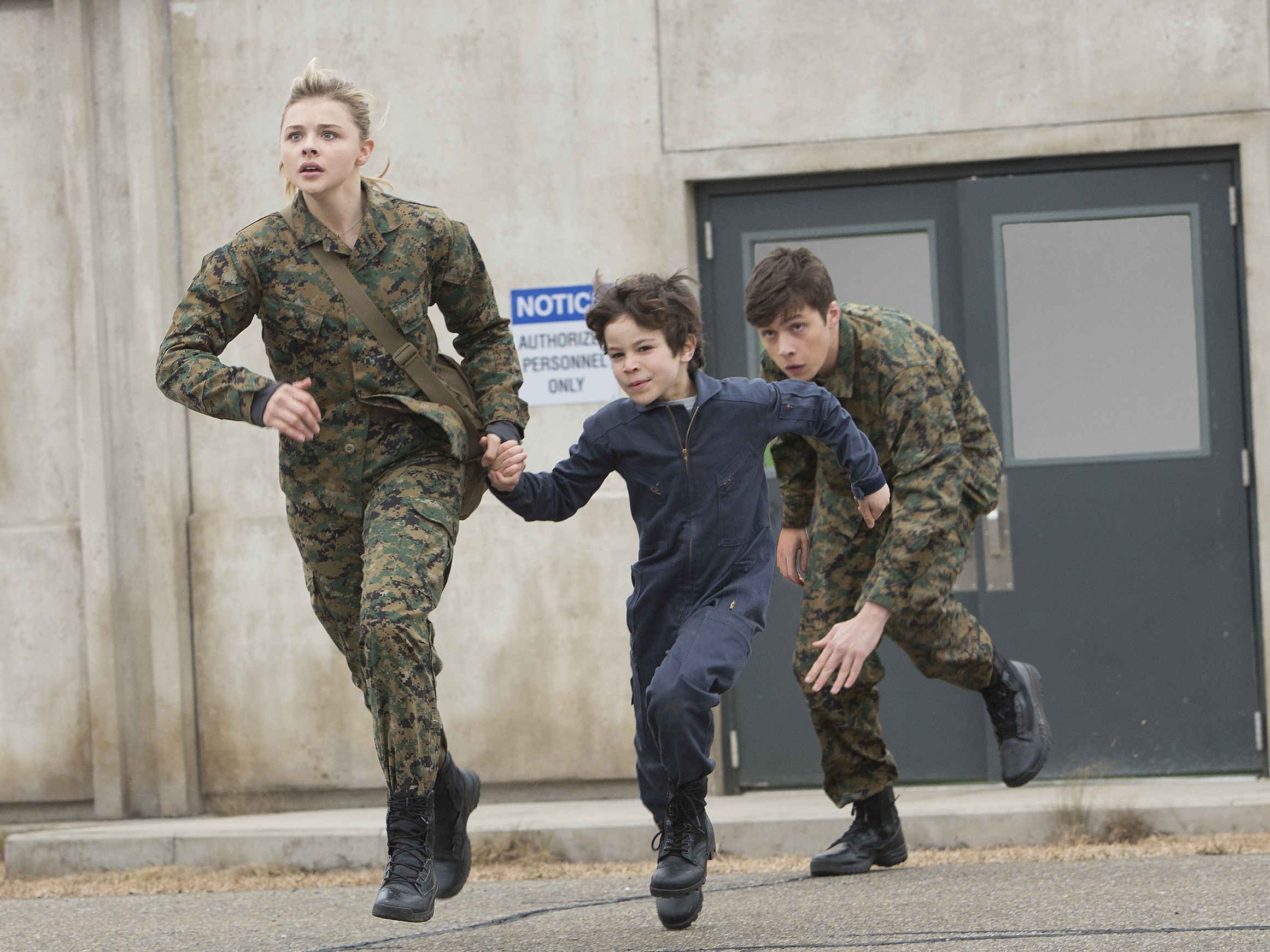 Cassie (ChloÃ« Grace Moretz) and Ben (Nick Robinson), wearing army fatigues, run with pre-teen Sam (Zachary Arthur)