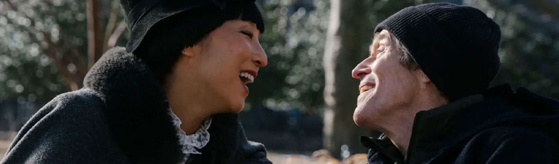 A woman and a man smile at each other while sitting on a park bench.