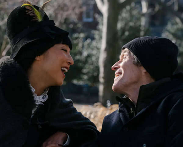 A woman and a man smile at each other while sitting on a park bench.
