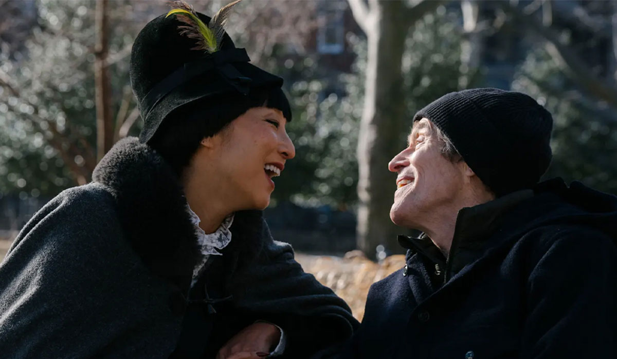 A woman and a man smile at each other while sitting on a park bench.